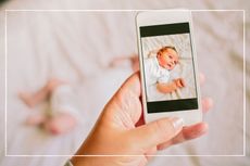 Mum taking a photo of infant on a bed using a smartphone