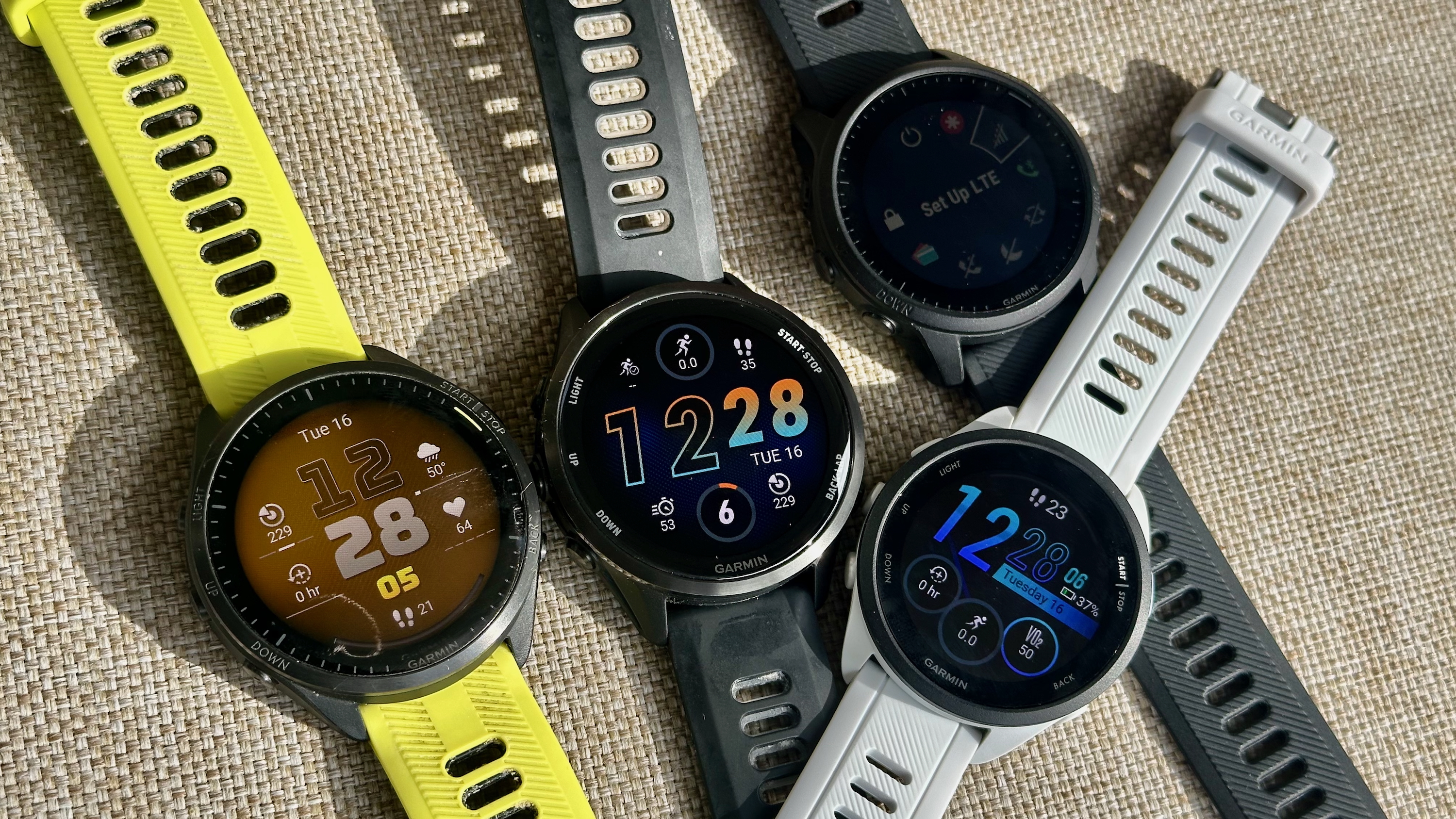 A photo of the Garmin Forerunner 965, 970, 945 LTE, and 165 sitting in a clump on a light canvas surface.