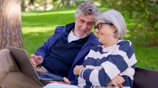 3D7HR34 Senior couple using a laptop outdoors in a park and celebrating good news