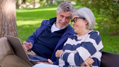 3D7HR34 Senior couple using a laptop outdoors in a park and celebrating good news
