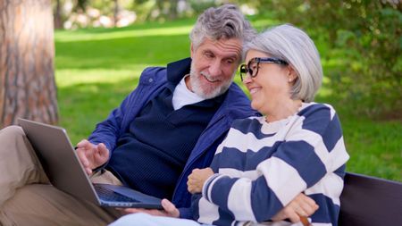 3D7HR34 Senior couple using a laptop outdoors in a park and celebrating good news