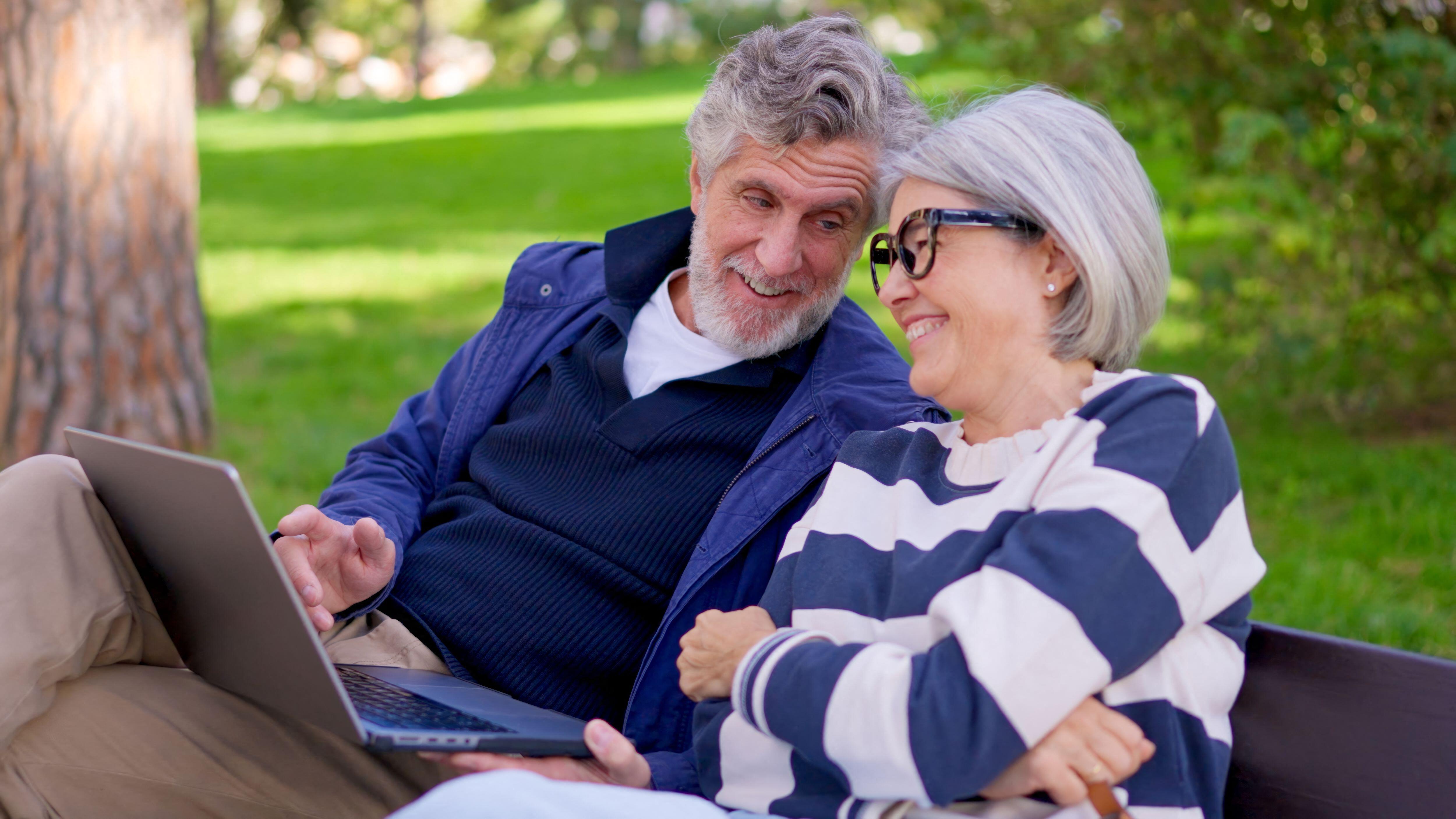 3D7HR34 Senior couple using a laptop outdoors in a park and celebrating good news