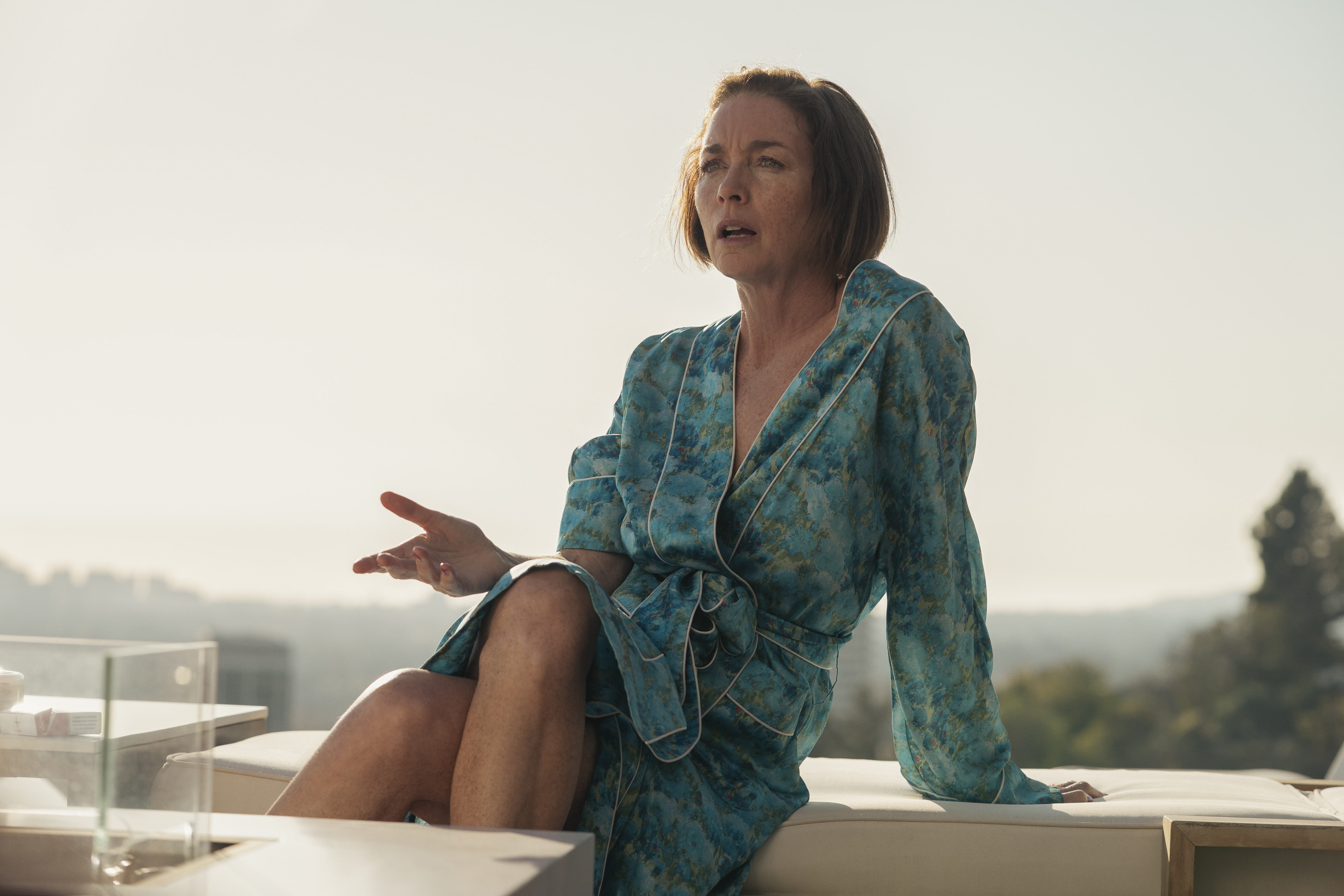 Dance Mom (Julianne Nicholson) wearing a robe and sitting outside, in 'Hacks' season 4.