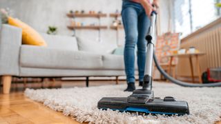Person wearing blue jeans using a vacuum cleaner on a fluffy rug.