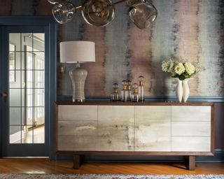 side cabinet with patterned wallpaper in muted colors with skirting boards painted dark blue