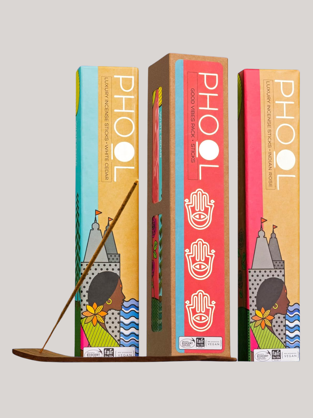 A set of three colorful patterned incense boxes beside a stick in a holder from PHOOL