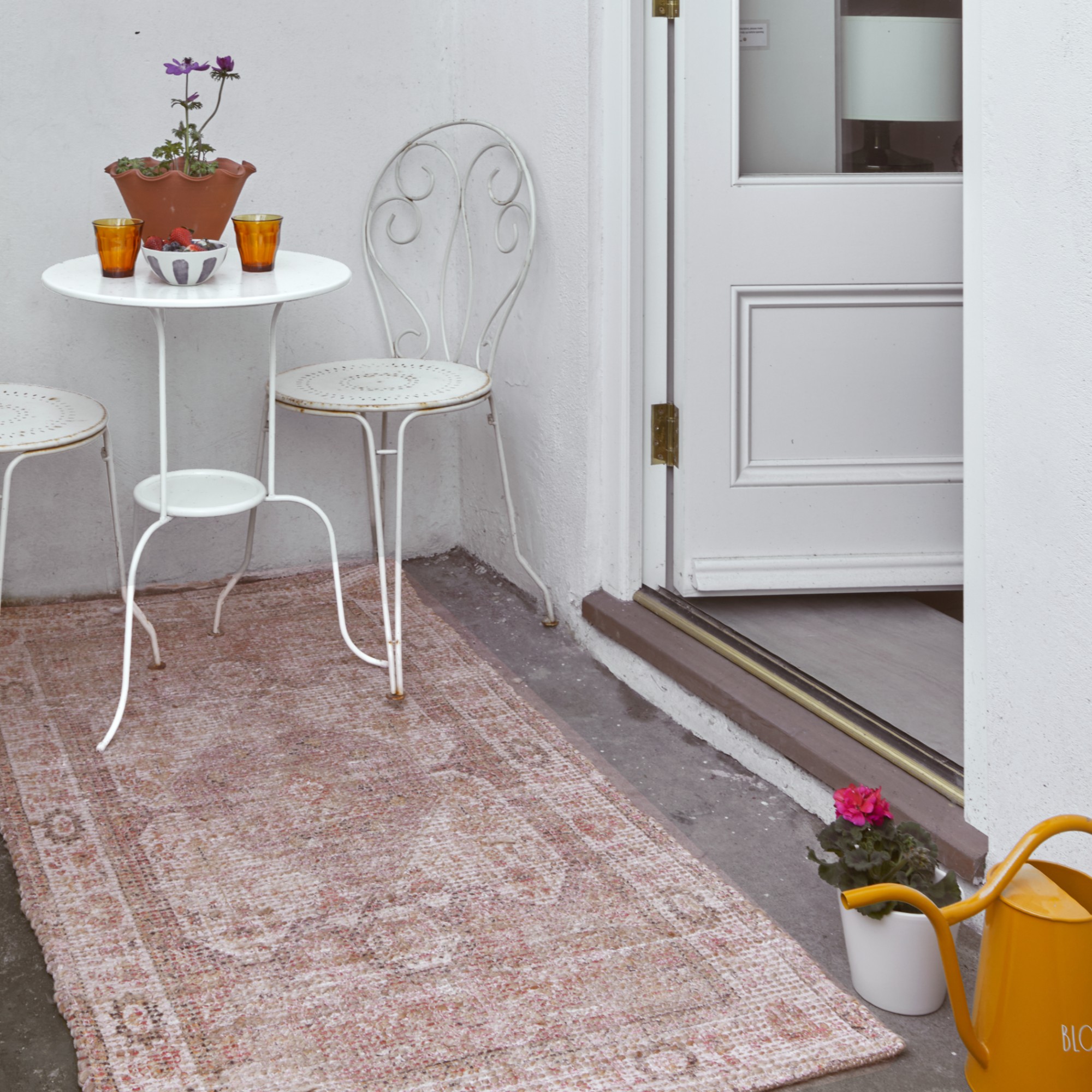 A small balcony with a white bistro set and the floor covered with a Moroccan-style outdoor rug