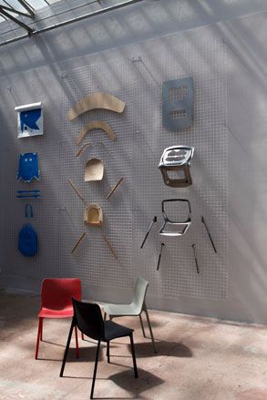 3 plastic chairs (red, grey and black) on display, next to a display of broken chairs on a grey wall