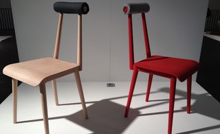 White platform and backdrop, a light wood chair and a red chair with black tubular back rest