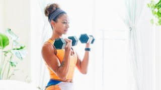 Woman performs biceps curl with dumbbells at home