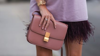 a hand wearing nude nail polish holding a bag