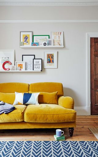 Floating shelving with different frames above yellow ochre two seater and geometric area rug