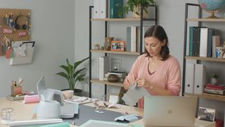Cricut Explore 3 vs Cricut Maker 3; a woman in a craft room using a Cricut machine and a laptop