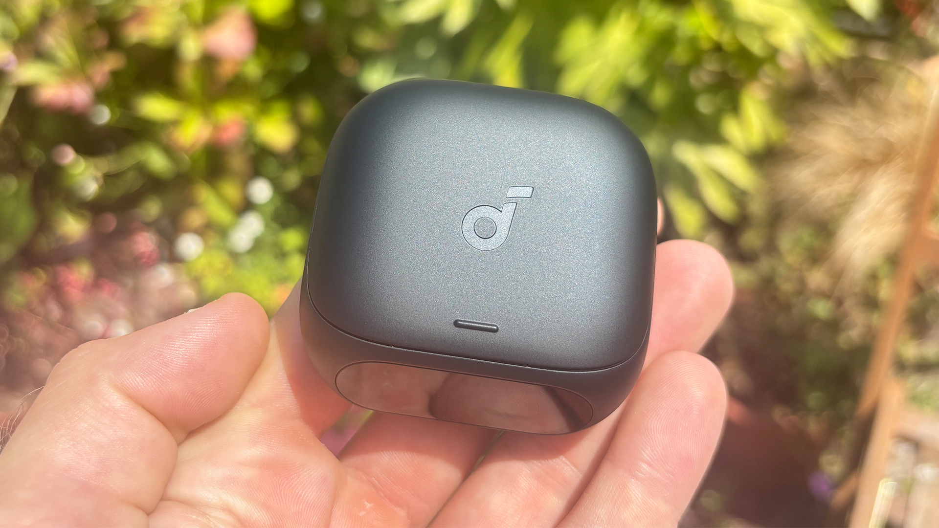 Soundcore Liberty 5 Pro in-ear headphones case held in hand in front of garden bush
