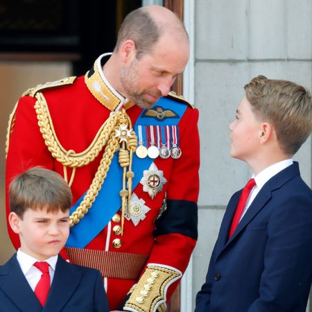 Prince William wearing a red uniform looking down at Prince George, who is smiling