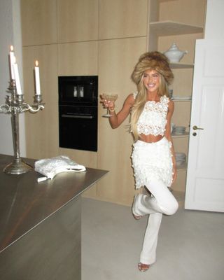 Emili Sindlev wearing an all-white outfit and furry hat at home