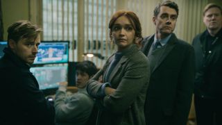 Jack Lowden and Olivia Cooke stand in a room of other confused colleagues in Slow Horses.