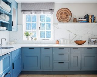 Blue kitchen cabinets with white worktops and marble back splashes