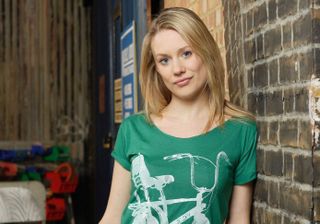 Carly Wicks leaning against a brick wall wearing a green t-shirt with a bike on it.