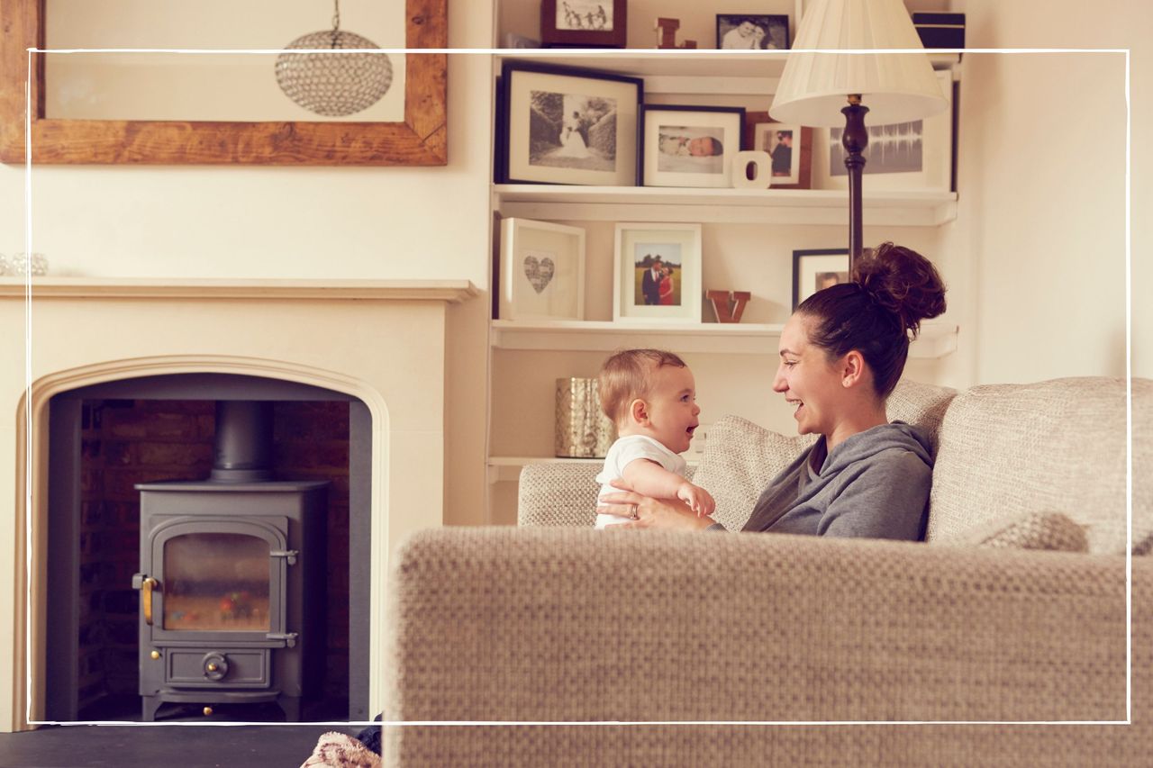 mother with baby on knee while sat on the sofa in front of an unlit fireplace