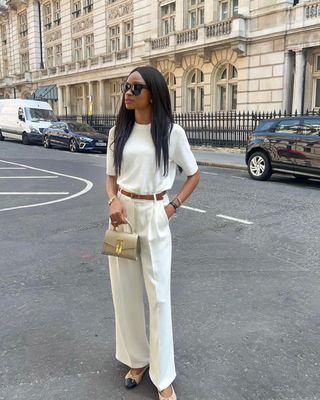 fashion influencer @symphonyofsilk wearing white trousers, a white knit top, and brown leather belt