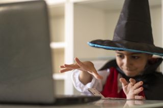 A young boy in a wizard hat and cape learning some magic tricks from Youtube with cards.