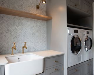 Bijoux laundry room design will off the floor washer dryer, tiled backsplash, and ceramic utility sink with brass taps