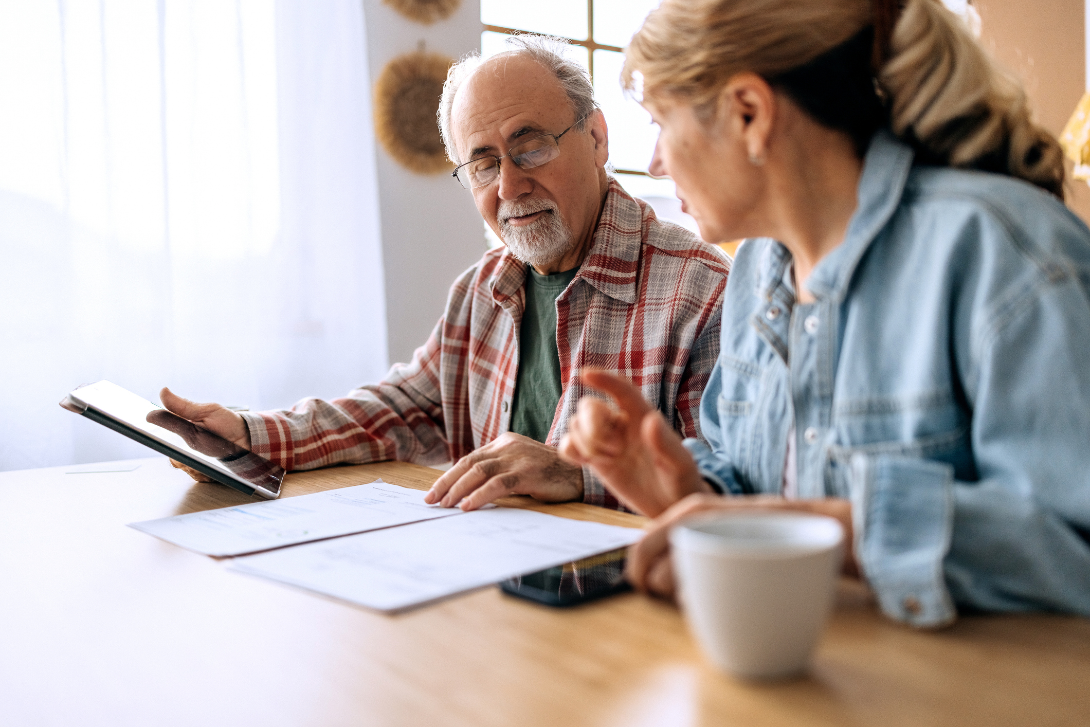 A mature couple sits together at home, reviewing expenses and bills. Their focused expressions reflect teamwork and financial planning in a comfortable setting.