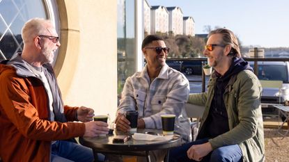 Three mature men socialize at a bar, sitting outdoors. They look like old friends.