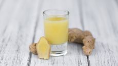 Shot glass filled with yellow liquid, with cut root ginger propped up against the glass