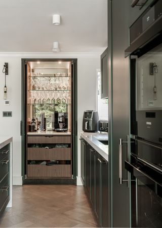 Dark green kitchen with a pocket door breakfast bar area with wooden drawers and glass shelves within