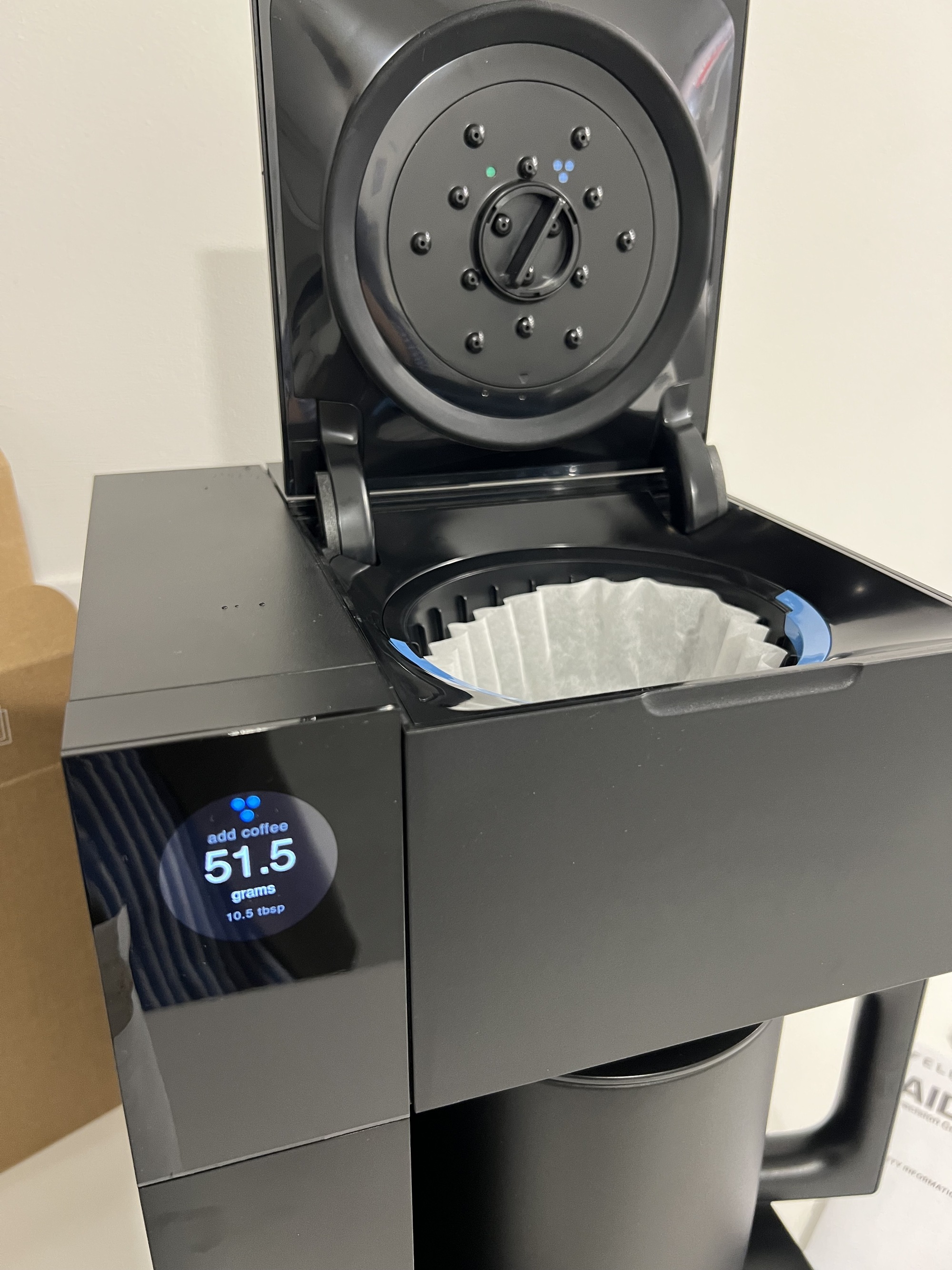 Image of a black drip coffee machine with the top compartment open with a paper filter in the machine.