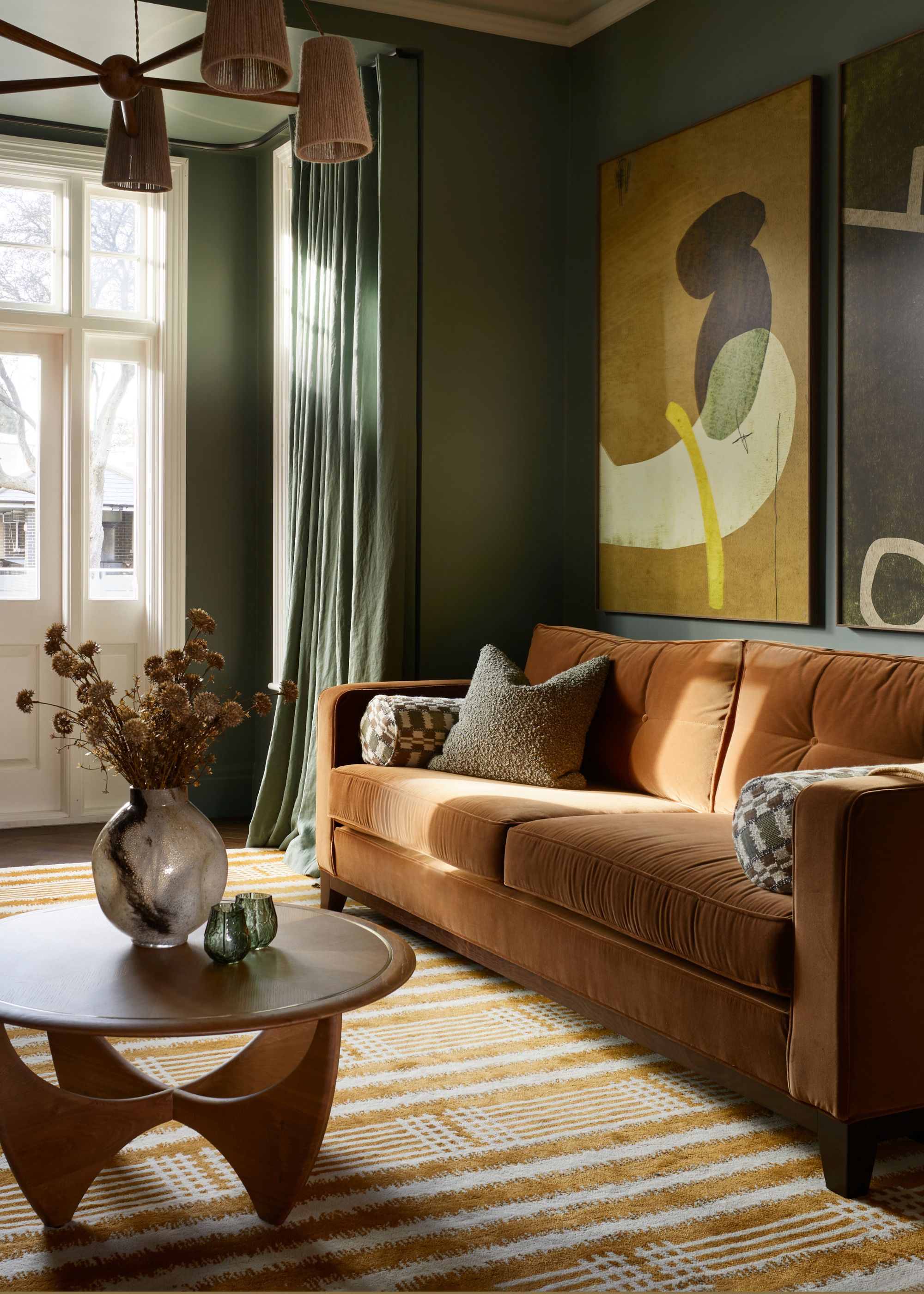 reception room with dark green walls, garden doors, striped rug and round coffee table with vase of flowers, rust-colored sofa and artwork on walls