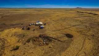 A photo of the site where paleontologists unearthed the skull shows several cars and a tent set up near a dig site on a vast plain