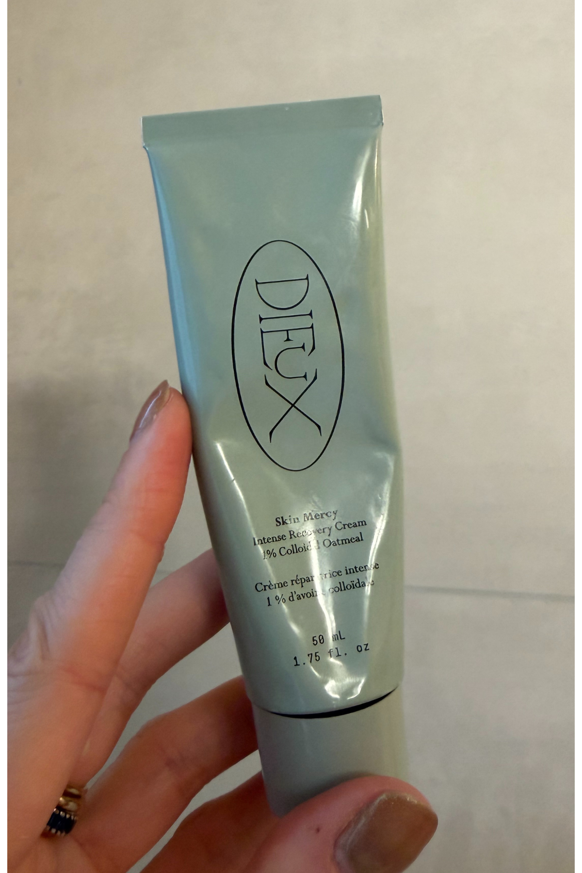 a hand holding a green bottle of dieux skin mercy cream
