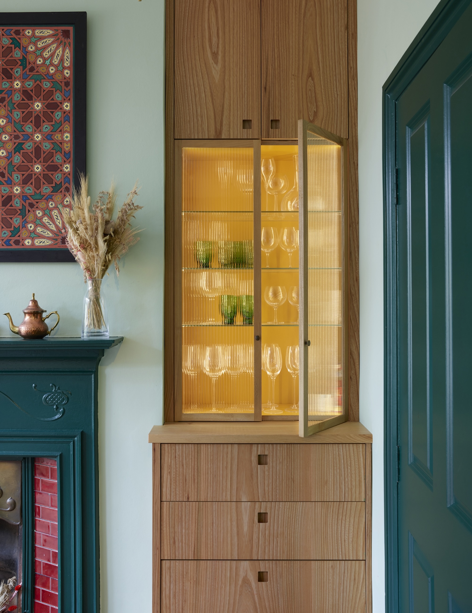 A fluted glazed cabinet with a bold yellow interior shown as part of a built-in wooden unit