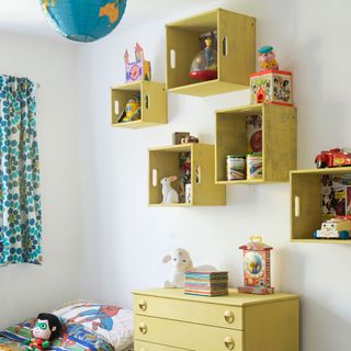 White wall with yellow painted box shelves and chest of drawers in a children's room
