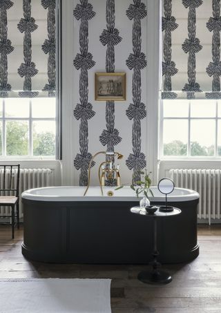 Ribbon printed wallpaper with matching blinds behind gray freestanding bath with silver plated faucets and wooden flooring