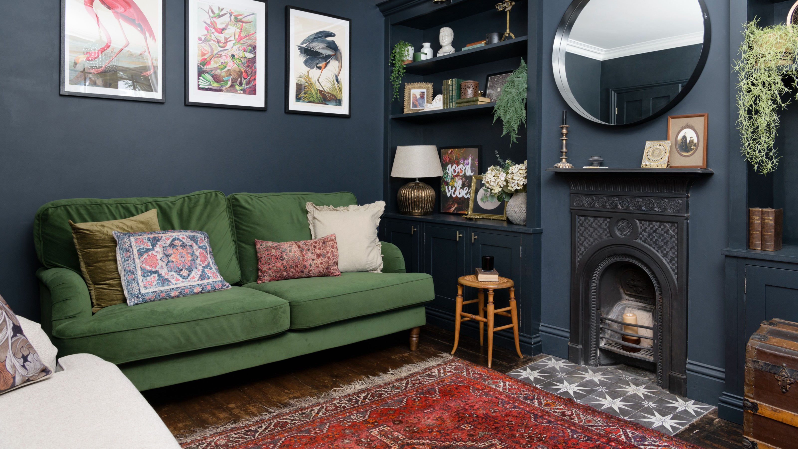 A living room painted in dark ink blue with a green velvet sofa