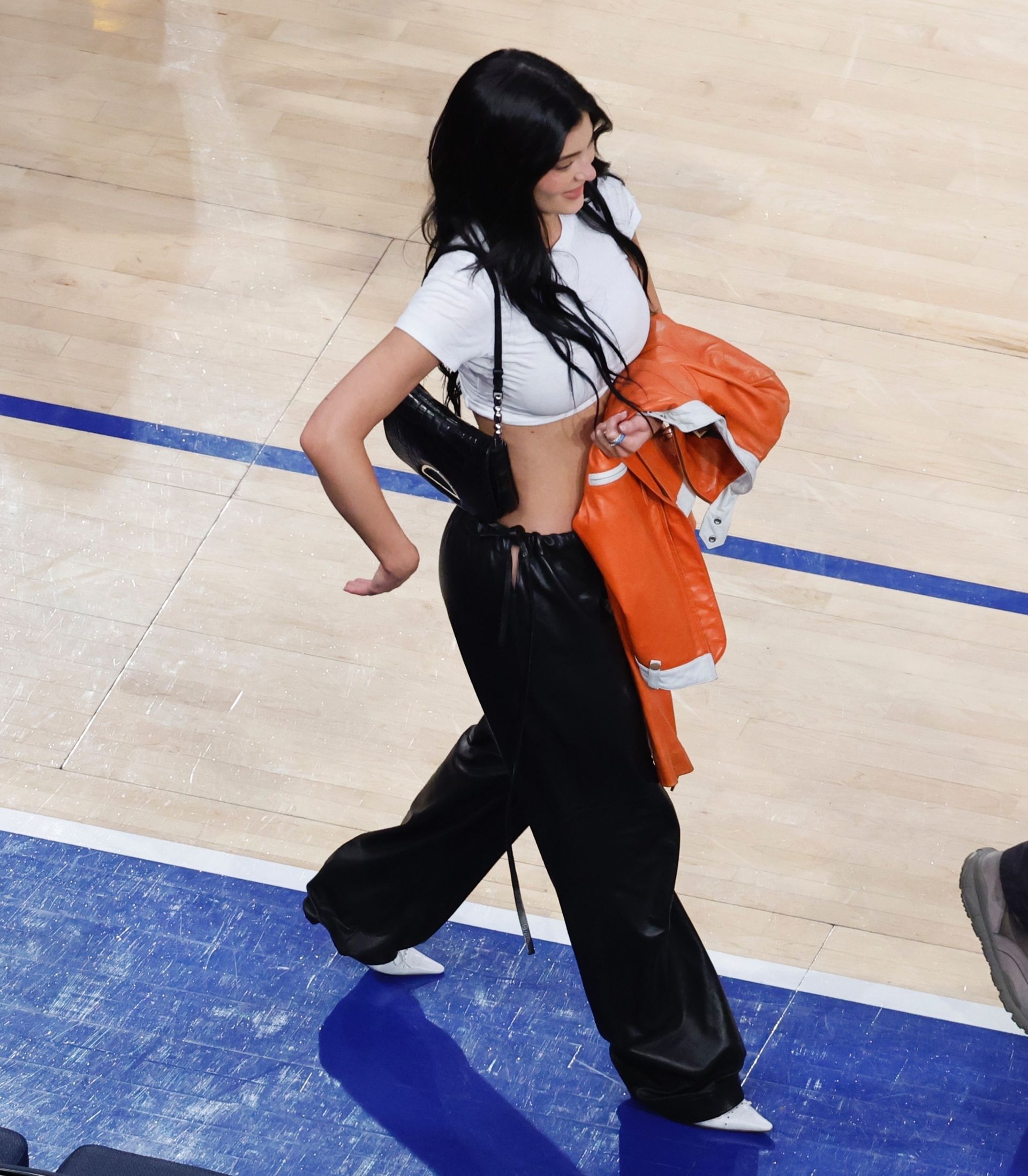 Kylie jenner wears a cropped white t-shirt, black leather pants, and white pointed toe heels.