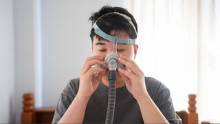 A man putting on a sleep apnea mask that covers his nose and mouth and straps around his head.