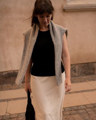 Senior fashion editor Halie LeSavage wears a black shirt with a white column skirt and a grey sweater over her shoulders for the Rotate show at Copenhagen Fashion Week