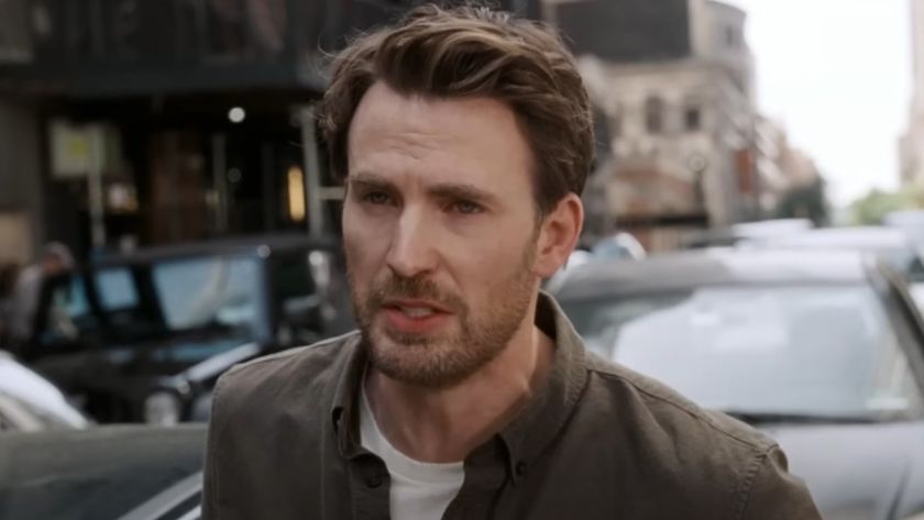 Chris Evans talking with cars behind him in Materialists. 
