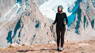 girl in thermal underwear with trekking poles walks along the trail among the snow-capped high peaks of the mountains