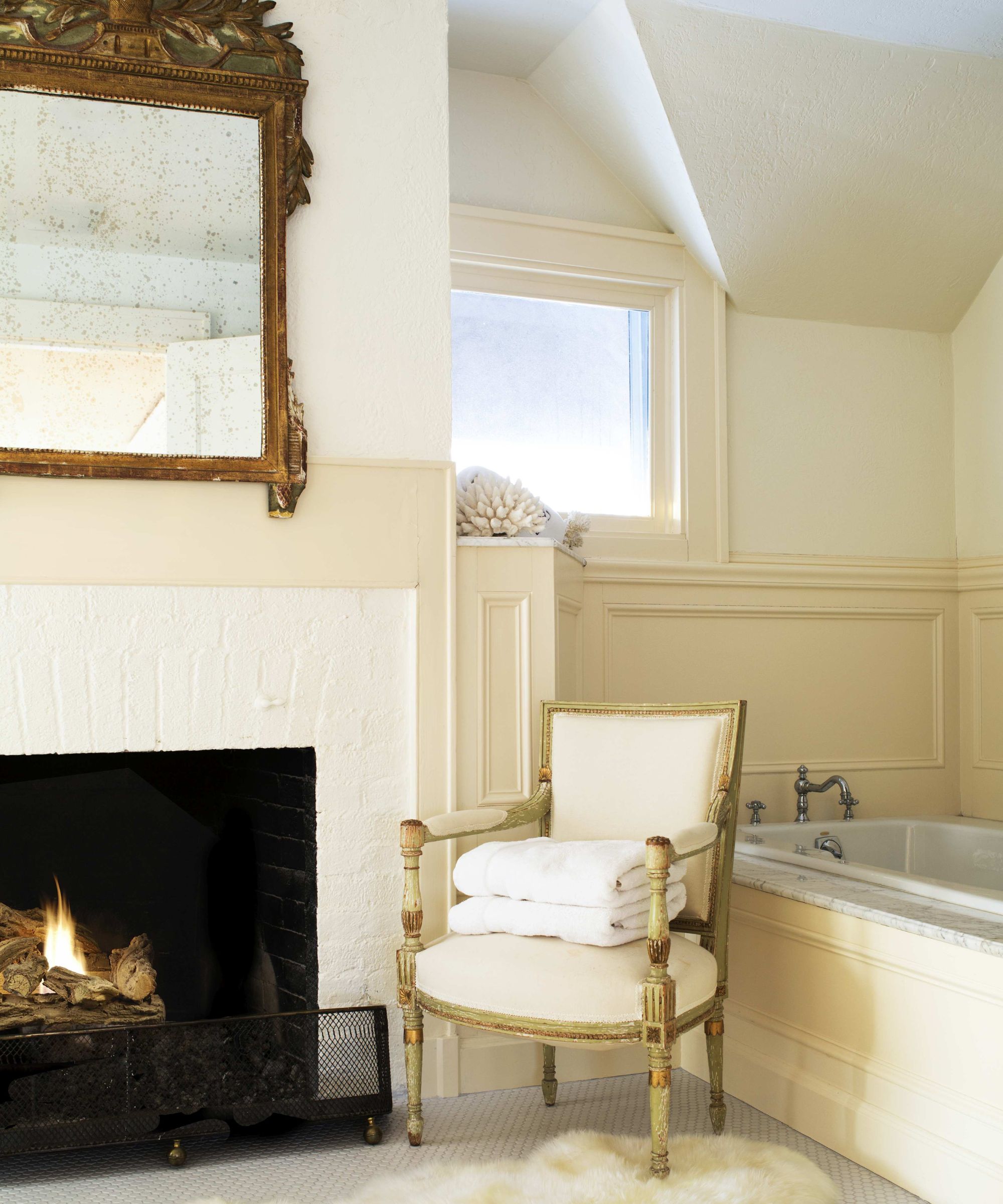 A charming traditional bathroom with a freestanding tub, open fireplace, antique mirror and classic panelling for a cosy, boutique feel.