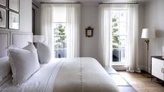 A white bedroom with a double bed and two tall windows