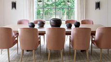 a dining room with a large wood table, ten pink dining chairs, and a carpet on the floor