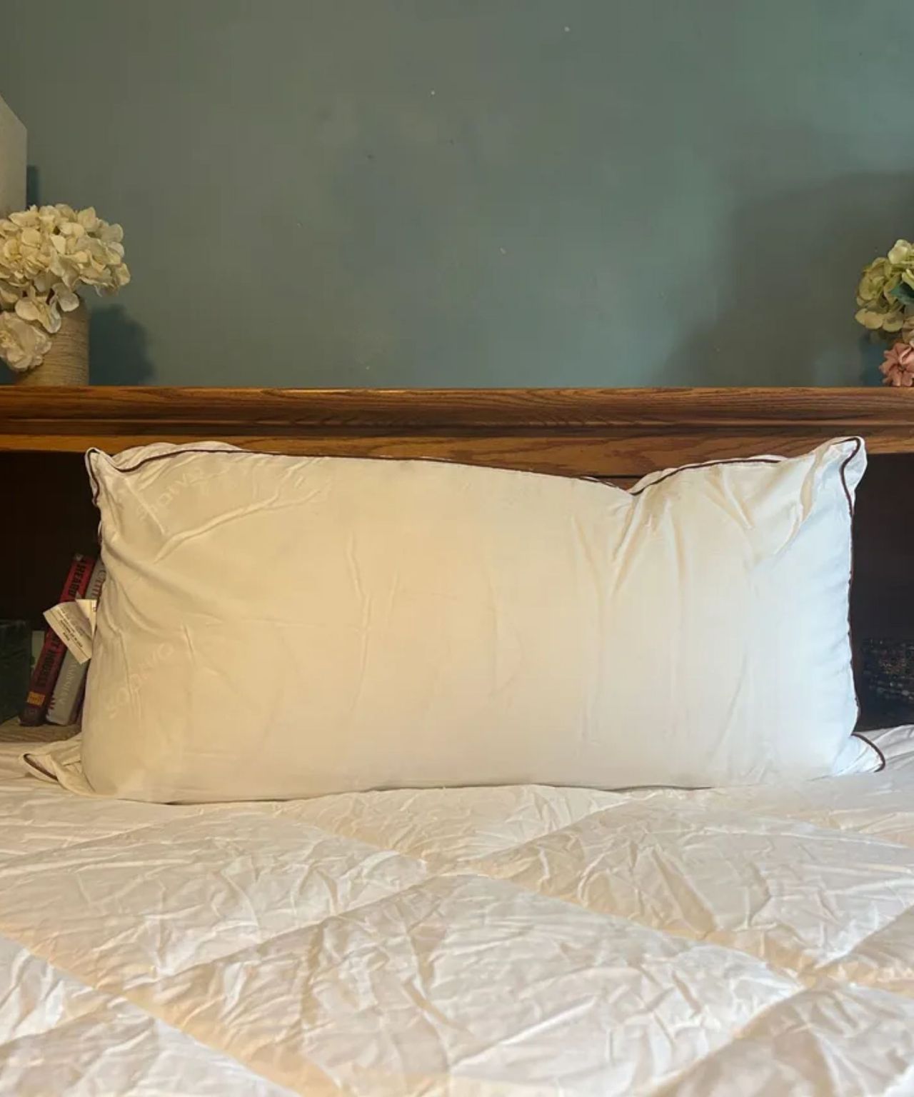 Saatva Latex Pillow on a bed with a wooden shelf and a teal wall behind
