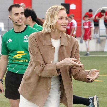 Princess Charlene wearing a brown jacket catching a ball