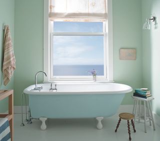 A bathroom with a free-standing tub painted in a pastel green-blue shade